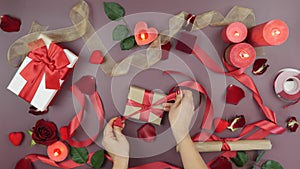 Hands are wrapping gift box with craft paper and red ribbon for St. Valentine`s Day. Woman is decorating gift box for present for