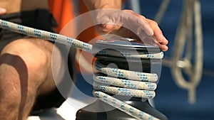 Hands of yachtsmen spooling rope to black bitts on the boat.