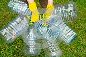 Hands in yellow gloves holding big empty plastic bottles. Grass on a background