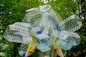 Hands in yellow gloves holding big empty plastic bottles. Grass on a background