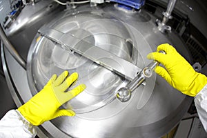Hands in yellow gloves opening industrial process tank