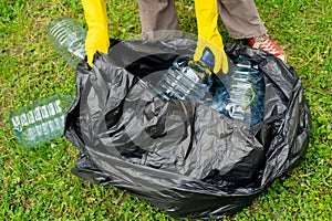 Hands in yellow gloves putting big plastic bottles into bllack plastic trash bag