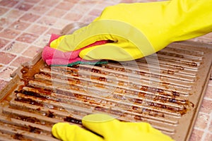 Hands in yellow household gloves remove grease from a dirty electric grill using a sponge and a special spray. Drops of fat after