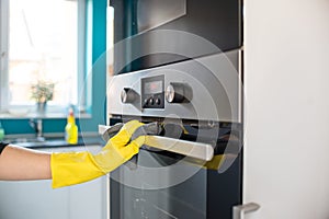 Hands in yellow protective rubber gloves cleaning oven