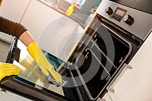Hands in yellow protective rubber gloves cleaning oven
