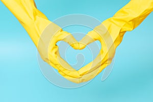 Hands in yellow rubber gloves in the shape of a heart on blue background