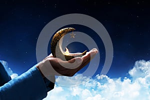 Hands of young asian muslim man hold shiny golden crescent moon with star lantern