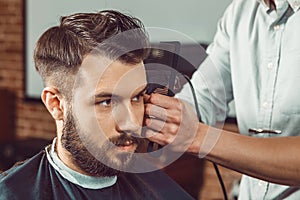 The hands of young barber making haircut to attractive man in barbershop