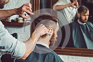 The hands of young barber making haircut to attractive man in barbershop