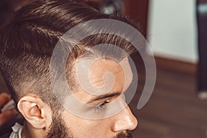 The hands of young barber making haircut to attractive man in barbershop