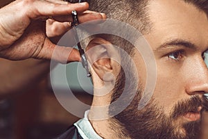 The hands of young barber making haircut to attractive man in barbershop