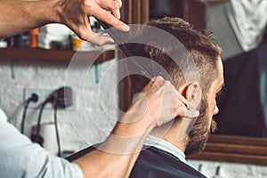 The hands of young barber making haircut to attractive man in barbershop