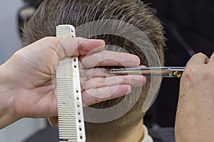 The hands of young barber making haircut to attractive man in barbershop. mens hair cutting scissors