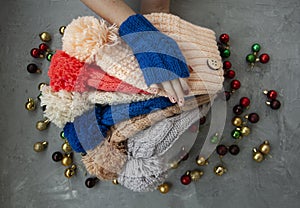 Hands of young beautiful woman in blue mittens holding many colored bright warm winter hats. On a gray background are bright