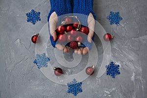 Hands of young beautiful woman in blue mittens. She holds Christmas red balls. Nearby are blue snowflakes and red decorations on