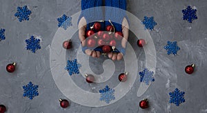 Hands of young beautiful woman in blue mittens. She holds Christmas red balls. Nearby are blue snowflakes and red decorations on