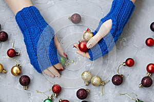 Hands of young beautiful woman in blue mittens with a pattern. She holds a green ball in one hand and a red and yellow ball in the