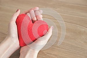 Hands of a young beautiful woman gently holding a red heart, on a wooden background, selective focus, save space.