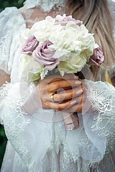 Hands of young bride holding beautiful wedding bouquet. Bride`s hand with a wedding ring on her finger. Bride in vintage white