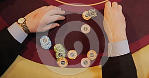 Hands of a young caucasian man playing poker in a casino. Close-up of hands playing poker with chips on red table.