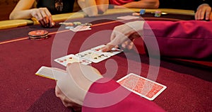 Hands of a young caucasian man playing poker in a casino. Close-up of hands playing poker with chips on red table.