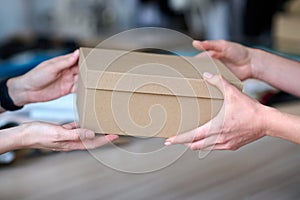 Hands of young craftswoman passing packed box with leatherwear to buyer