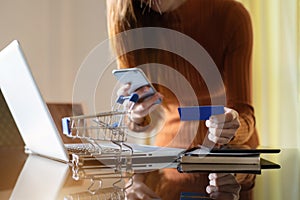 Hands of young female holding smartphones and using credit cards and laptop computers.