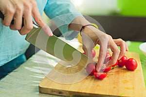 Hands of a young girl chop the cherry tomatoes on a wooden cutting board on a green table in a home setting