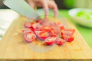 Hands of a young girl chop the cherry tomatoes on a wooden cutting board on a green table in a home setting