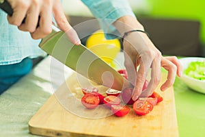 Hands of a young girl chop the cherry tomatoes on a wooden cutting board on a green table in a home setting