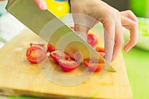 Hands of a young girl chop the cherry tomatoes on a wooden cutting board on a green table in a home setting