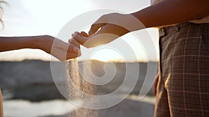 The hands of a young girl and a guy pour sand from the beach at sunset. Sea sand in a man& x27;s hand. man& x27;s hand