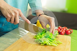 Hands of a young girl slice green lettuce leaves on a wooden cutting board on a green table in a home setting against a