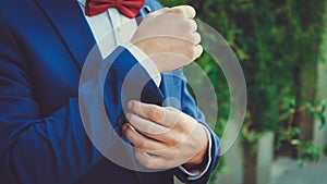 Hands of a young man in a blue suit with a red bow tie