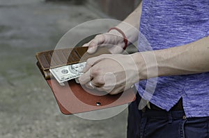The hands of a young man of European ethnicity remove a five-dollar bill from a purse