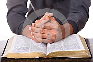 Hands of a young man folded praying over a Bible, hands over soft focus Bible