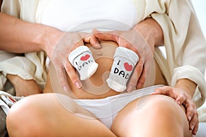 Hands of young man holding a par of socks on belly of his pregnant wife at home photo