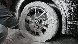 Hands of young man holding special cleaning glove, washing car wheel with foam. Cleaning of modern rims of luxury car at