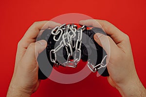 Hands of a young man holds a game controller is tied by chain, concept of game addiction