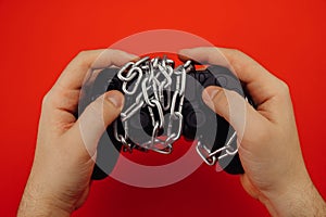 Hands of a young man holds a game controller is tied by chain isolated on red background