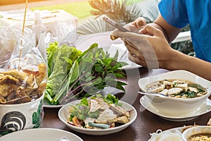 Hands of young man play a game with smart phone before eat pork sausage spicy salad Thai and Vietnam food (Yum Moo Yor)