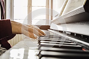 Hands of a young man playing piano reading a score at the sunlight