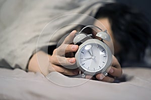 Hands of a young man from under the blankets hold a retro vintage alarm clock.