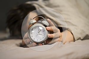 Hands of a young man from under the blankets hold a retro vintage alarm clock.