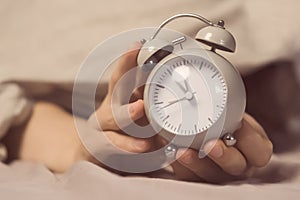 Hands of a young man from under the blankets hold a retro vintage alarm clock.