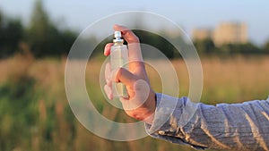 Hands of a young man using perfume at sunset