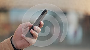 Hands of young man using smartphone in the street near shopping mall. Communication, online shopping, chat, social