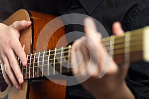 The hands of a young musician playing an acoustic guitar with metal strings close-up with a blurred background