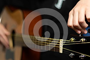 The hands of a young musician playing an acoustic guitar with metal strings close-up with a blurred background