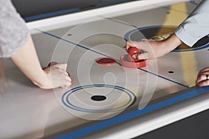 Hands of young people holding striker on air hockey table in game room